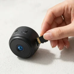 Ръка поставя MicroSD карта в слота на черна мини WiFi камера, подчертавайки възможността за локално съхранение на записите, надеждна защита и вашето пълно спокойствие.