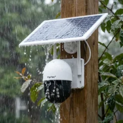 Външна безжична соларна камера FipTec със соларен панел, монтирана на дървена греда под силен дъжд, показваща безкомпромисна водоустойчивост и надеждна защита за вашето пълно спокойствие при всяко време.