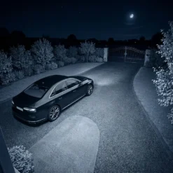 Изглед от външна безжична камера FipTec с нощно виждане, обхващащ паркиран автомобил и алеята към входната порта през нощта, предоставяйки надеждна защита и пълно спокойствие за вашия имот.