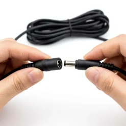 Човешки ръце свързват професионален DC захранващ удължителен кабел FipTec за охранителни камери на бял фон. Лесната инсталация гарантира надеждна сигурност за вашия дом и пълно спокойствие за семейството.