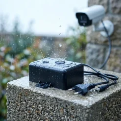 Водоустойчив захранващ адаптер FipTec, поставен под дъжда до охранителна камера, осигуряващ надеждна защита и захранване на вашата система за видеонаблюдение за пълно спокойствие и безопасност на дома.