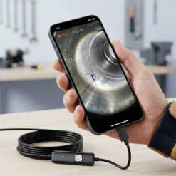 Смартфон в ръка, свързан към ендоскопска камера FipTec, показва на екрана детайлна инспекция на метална част с пукнатина в работна среда, демонстрирайки прецизност, надеждна защита и вашето пълно спокойствие.