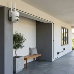 Бяла външна WiFi камера FipTec, монтирана на стена на модерна веранда с дискретно прекаран дълъг захранващ кабел. Осигурете надеждна защита на дома и пълно спокойствие за вашето семейство и имот.