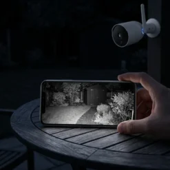 Бяла външна смарт WiFi камера FipTec, предаваща кристално инфрачервено нощно виждане на заден двор директно към смартфон в ръцете на потребител. Осигурете си надеждна охрана и интелигентна сигурност за вашето пълно спокойствие през цялото денонощие.