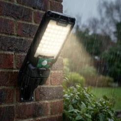 Водоустойчива соларна LED лампа FipTec, монтирана на тухлена стена, светеща ярко по време на силен дъжд. Надеждна външна охрана, която осигурява пълна защита и дискретна сигурност за вашето семейство.