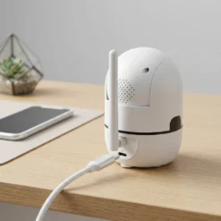 Бяла вътрешна Wi-Fi камера FipTec, свързана с плетен USB-C кабел за захранване върху дървено бюро. Дискретната сигурност осигурява надеждна защита на дома и пълно спокойствие с лесен контрол.