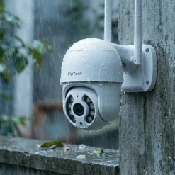 Водоустойчива WiFi камера от системата FipTec Protect 4, монтирана на външна бетонна стена под дъжда. Здравият корпус осигурява надеждна защита и пълно спокойствие за имота ви при всякакво време.