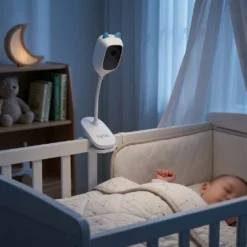 Бял смарт бебефон FipTec с щипка, монтиран на ръба на бебешко легло в тъмна стая, осигуряващ безжично наблюдение с нощно виждане за пълна сигурност и спокойно съзнание на родителите.