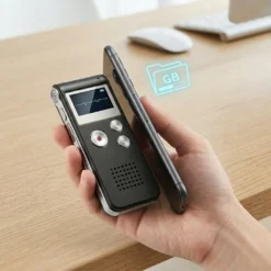 Човешка ръка държи компактен цифров диктофон FipTec VRS до смартфон върху дървено бюро, илюстрирайки лесен трансфер на данни. Дискретна сигурност и надеждна защита за вашето пълно спокойствие и лесен контрол.