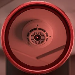 Близък план през червения визьор на детектор FipTec XScan LM10, който разкрива обектив на камера чрез светлинно отражение. Този уред гарантира пълна защита и дискретно спокойствие за вашето семейство.